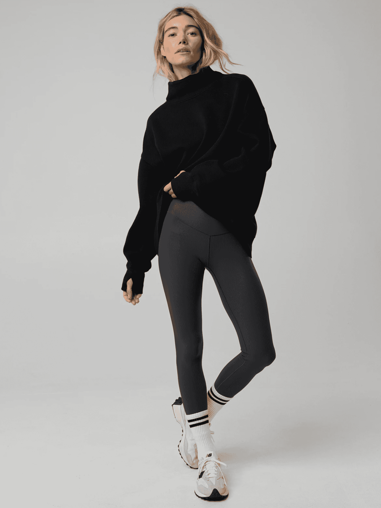 Person in black sweater and leggings poses with sneakers and striped socks.