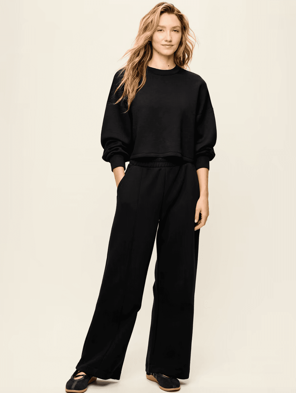 Person in black sweatshirt and pants, standing on a light background.