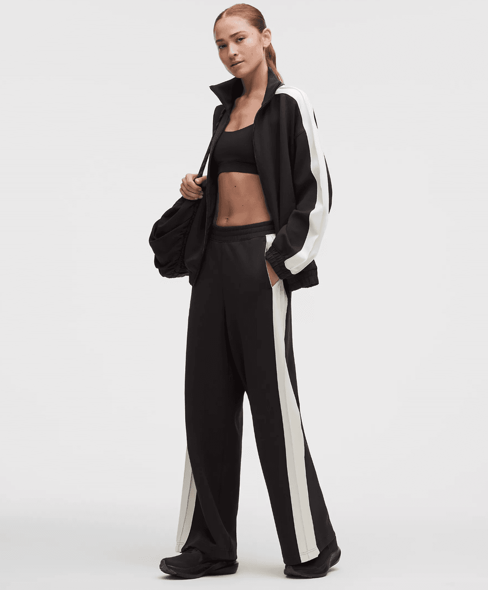 Person in black tracksuit with white stripes, black sports bra, and bag.