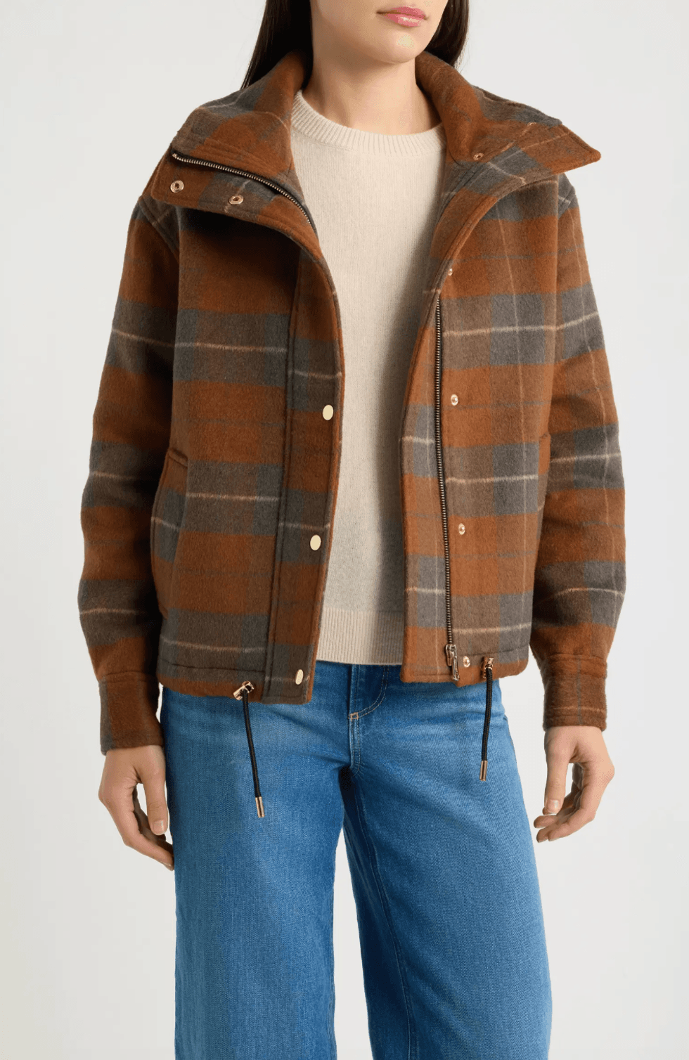 Person in brown plaid jacket, beige sweater, and blue jeans.
