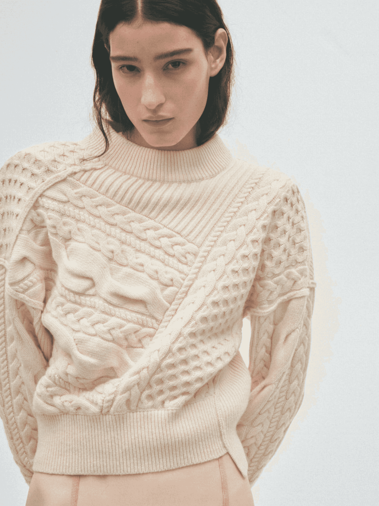 Person in cream textured sweater and beige skirt against a light background.