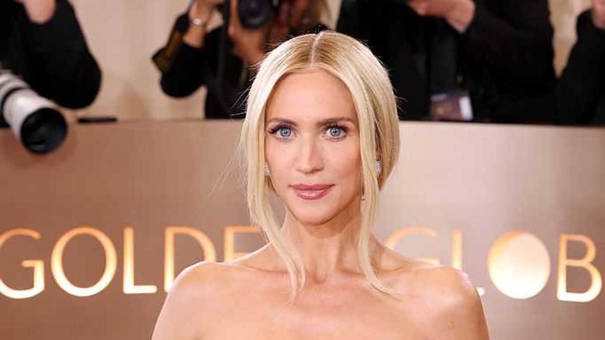 Person in elegant white dress at Golden Globes event, photographers in the background.