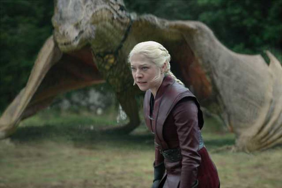 Person in front of a dragon with open wings in a forest setting.