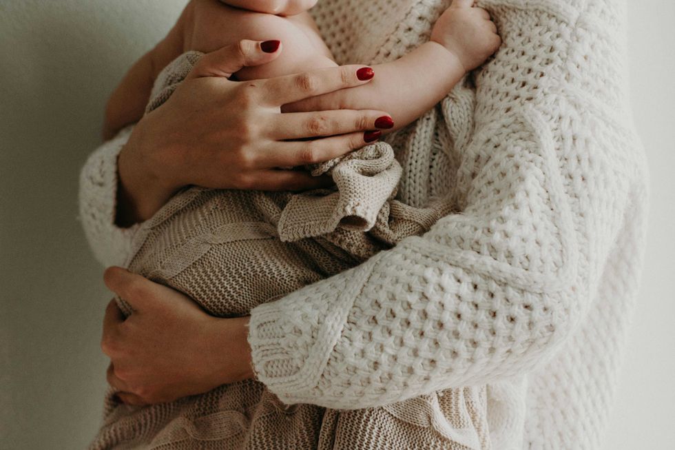 Person in knit sweater cradles a baby wrapped in a cozy beige blanket.