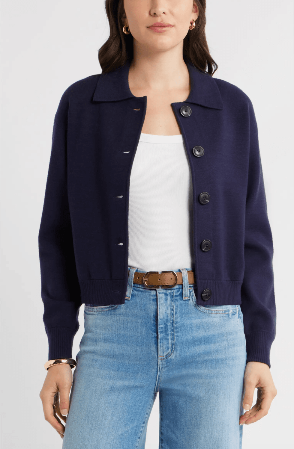 Person in navy cardigan, white tank, light jeans, and brown belt, standing with hands visible.