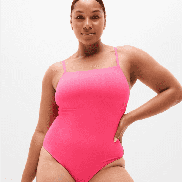 Person in pink one-piece swimsuit standing confidently against a plain background.