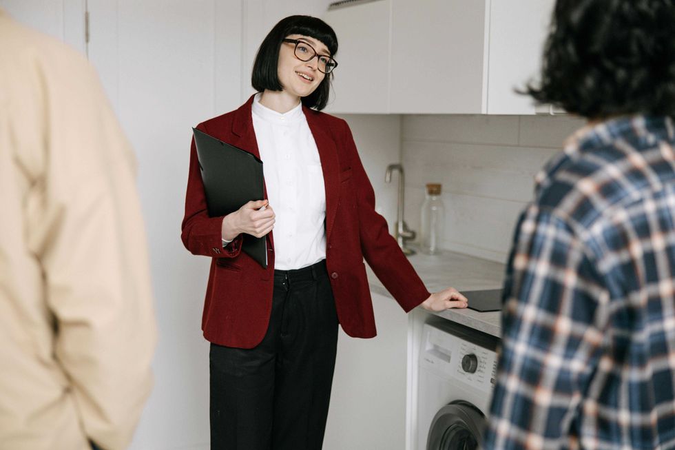 Person in red blazer showing a washer to two others in a modern room.