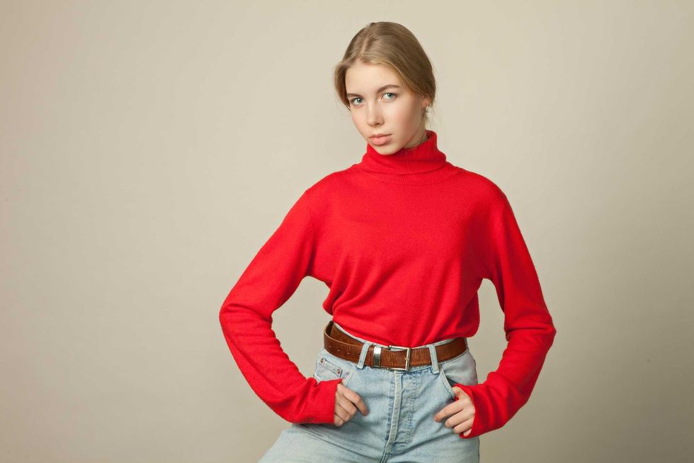 Person in red turtleneck and jeans poses against a plain background.