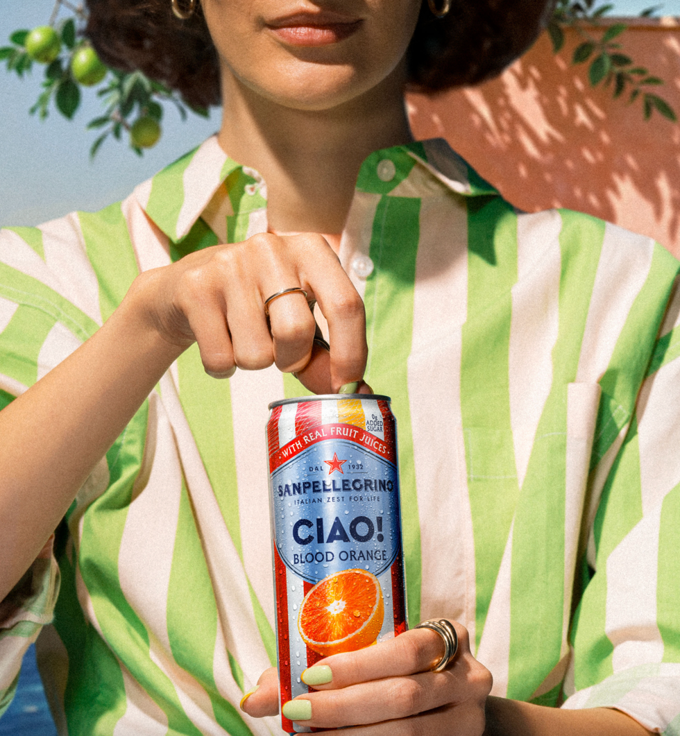 Person in striped shirt opening Sanpellegrino Blood Orange can outdoors.