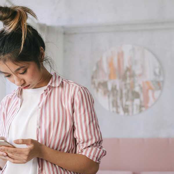 Person in striped shirt using a smartphone in a softly lit room.