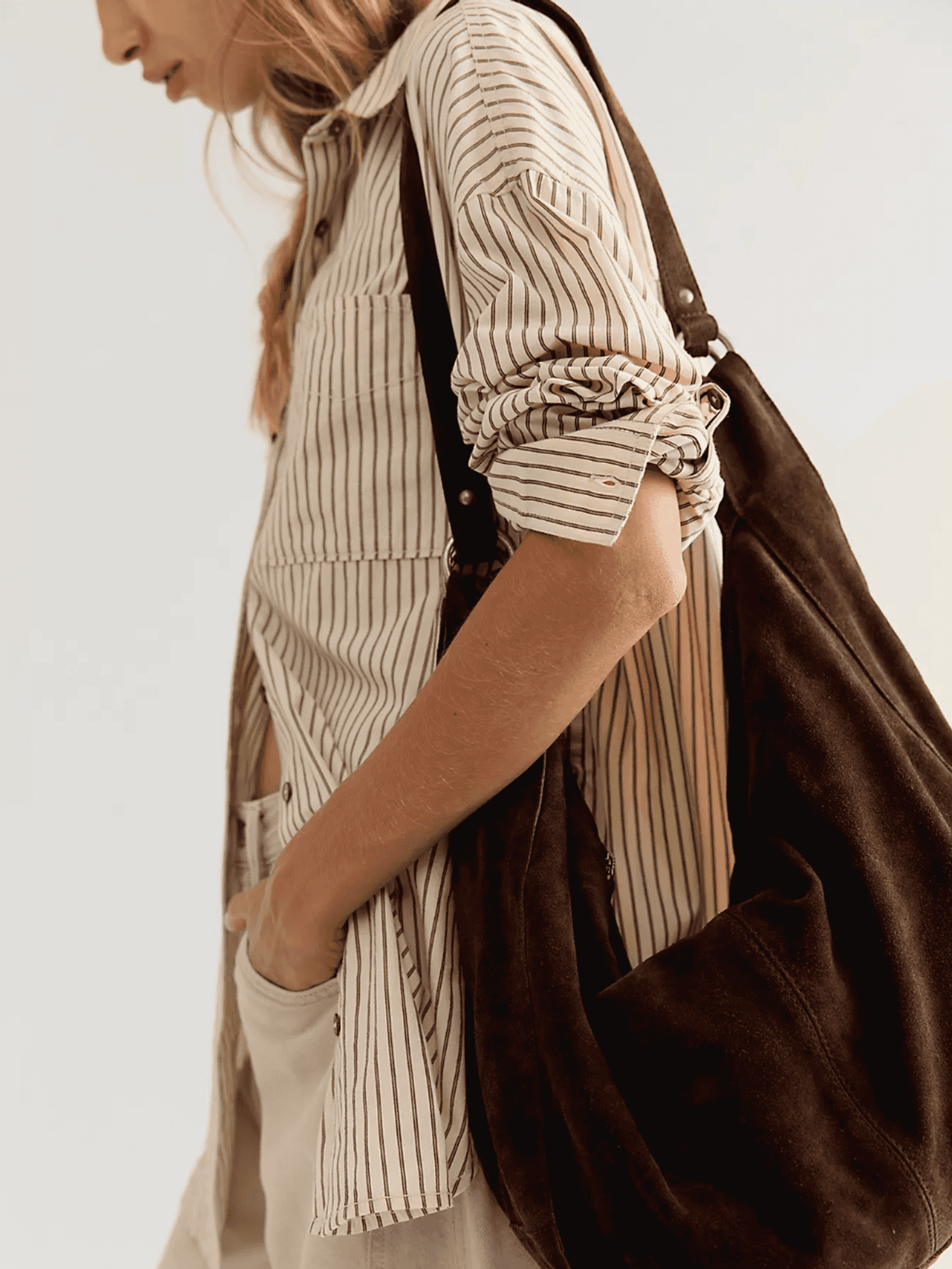 Person in striped shirt with a black bag and hand in pocket, facing sideways.