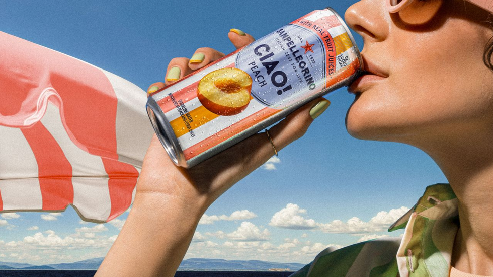 Person in sunglasses drinks a peach-flavored Sanpellegrino under a sunny sky.