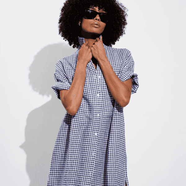 Person in sunglasses wearing a blue checkered shirt dress against a white background.