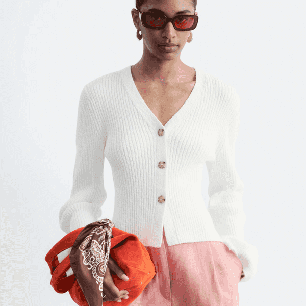 Person in white cardigan holding orange bag with bandana, wearing red sunglasses.