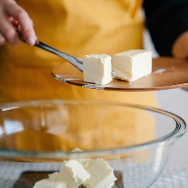 Person in yellow apron placing butter cubes into a glass bowl.