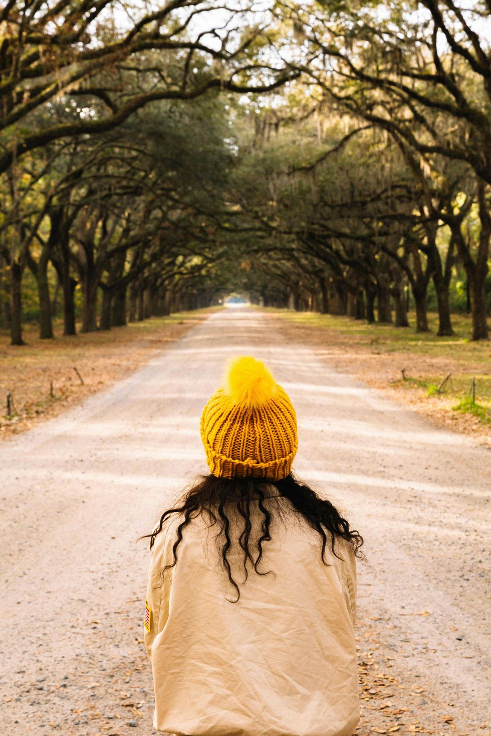Person in yellow hat on tree-lined dirt road.