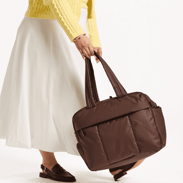 Person in yellow sweater holding large brown bag, wearing white skirt and loafers.