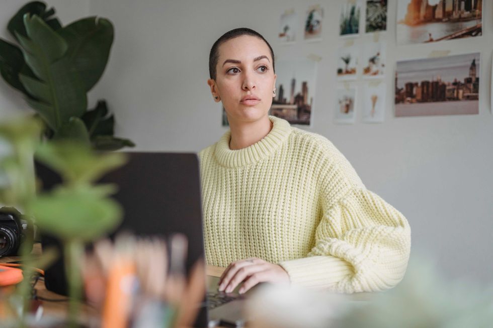 Person in yellow sweater sitting at a desk with laptop, looking away from camera.