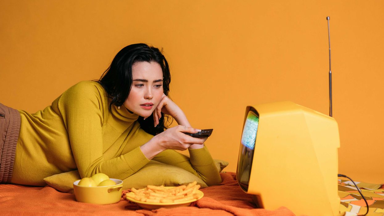 Person in yellow watches vintage TV, holding remote, surrounded by lemons and fries.
