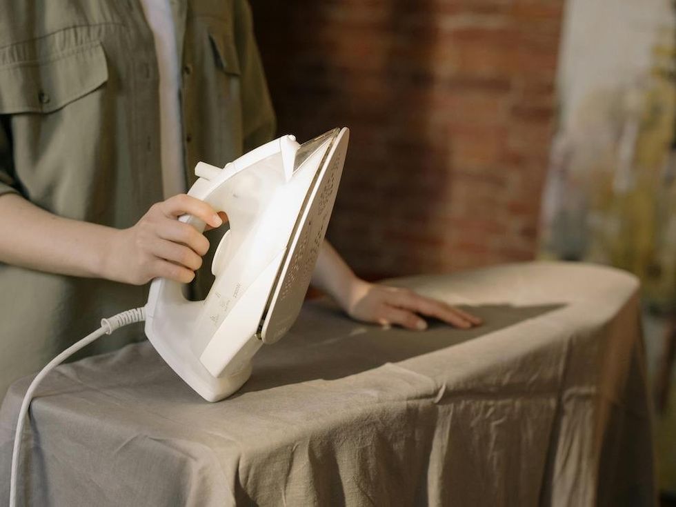 Person ironing a sheet on a board with a white iron.