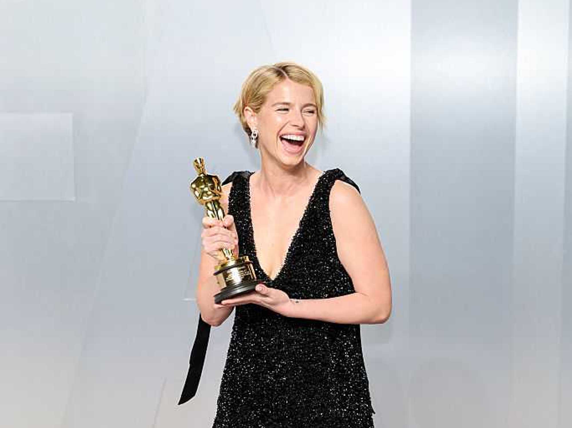 Person joyfully holding an Oscar trophy in a sparkling black dress.