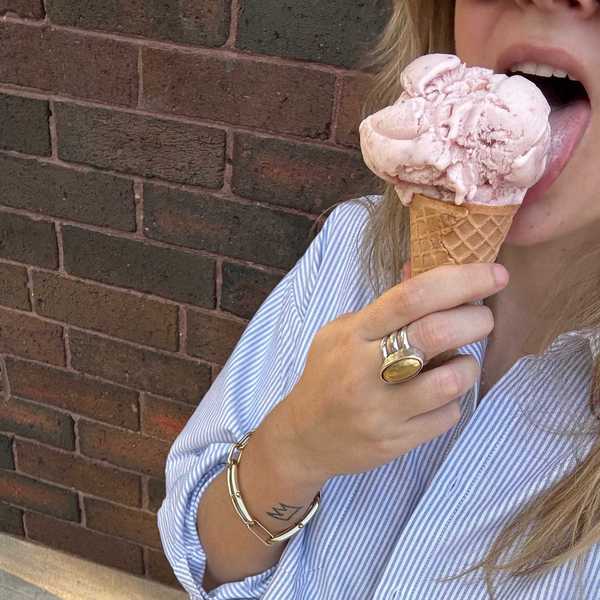 Person licking a strawberry ice cream cone against a brick wall background.