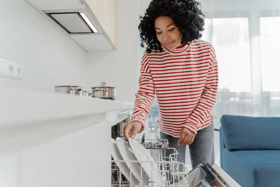Person loading a dishwasher with plates in a modern kitchen.