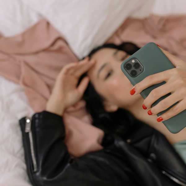 Person lying on bed, holding a phone with painted nails.