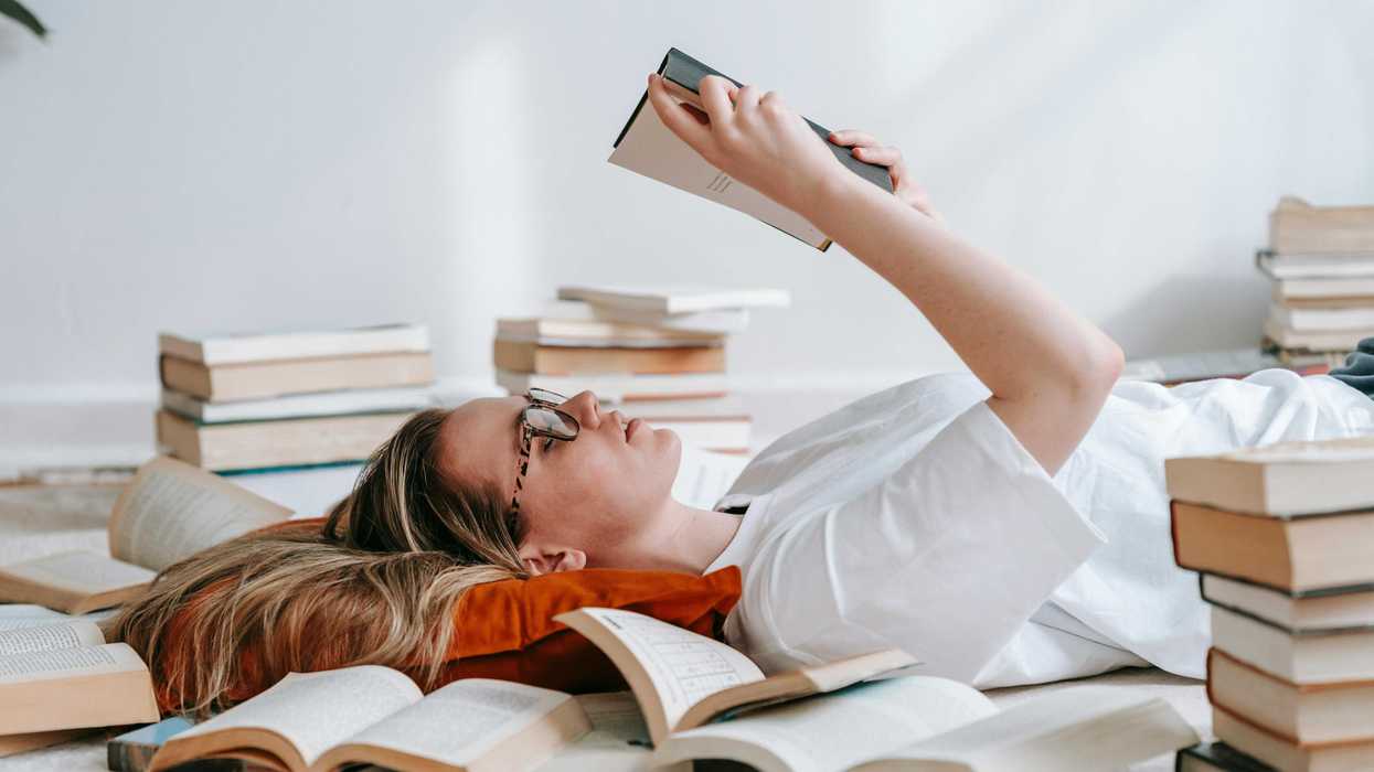 Person lying on the floor, reading a book, surrounded by piles of open and closed books.