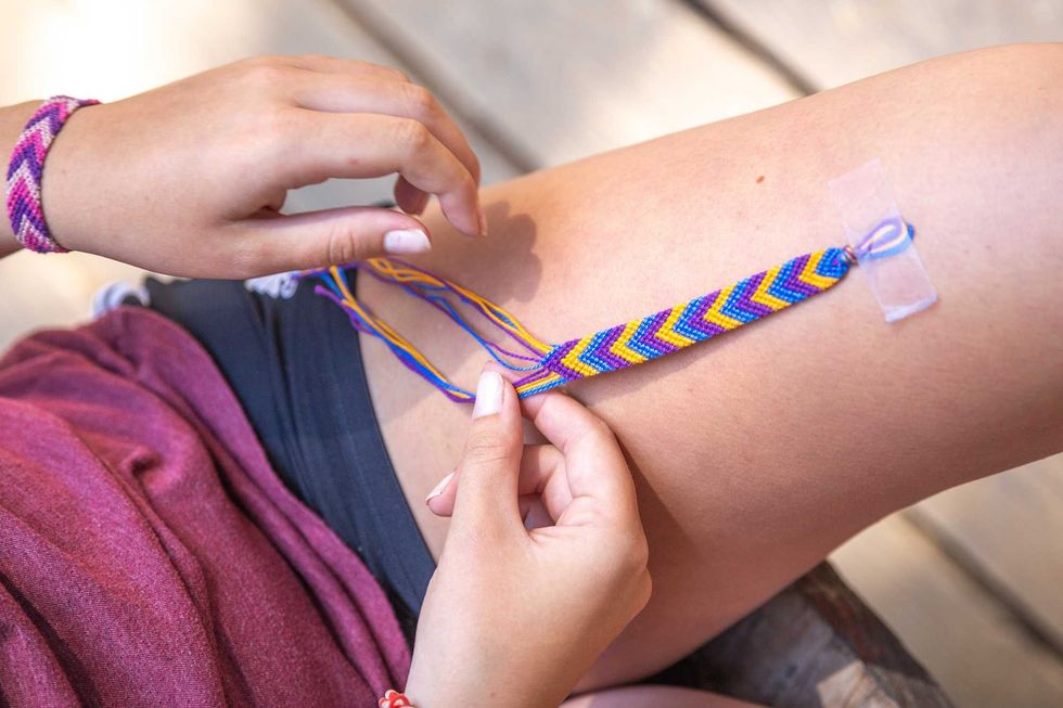 Person making a colorful chevron friendship bracelet on their knee.