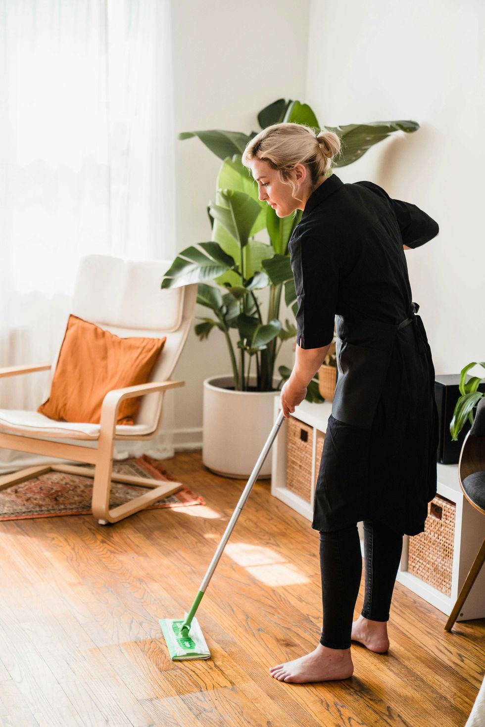 Person mopping wooden floor in bright room with plants.