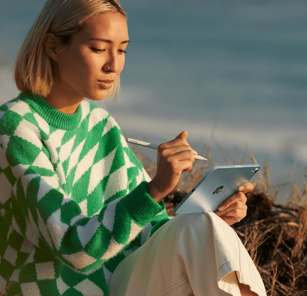 Person outdoors using a stylus on a tablet, wearing a green and white sweater.