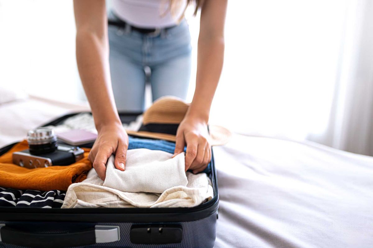 Person packing a suitcase with clothes and a camera on a bed.