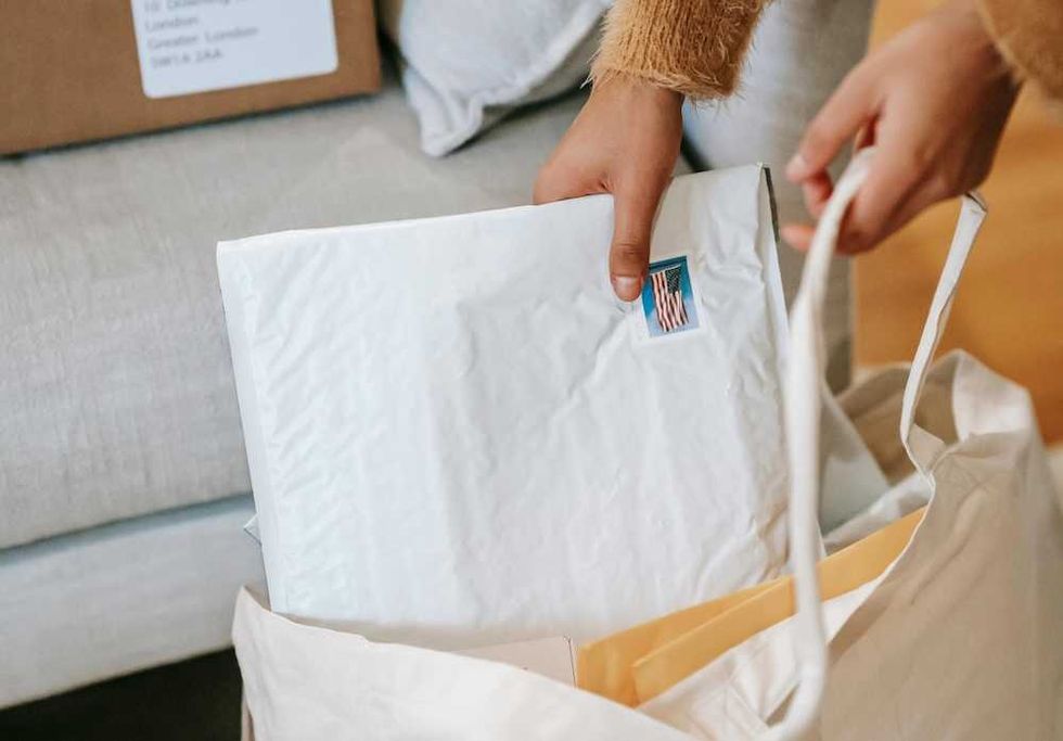Person placing a padded envelope with a stamp into a tote bag.