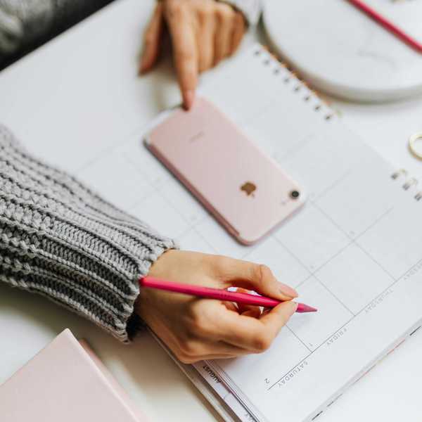 Person planning on a calendar with a pink phone and pen.