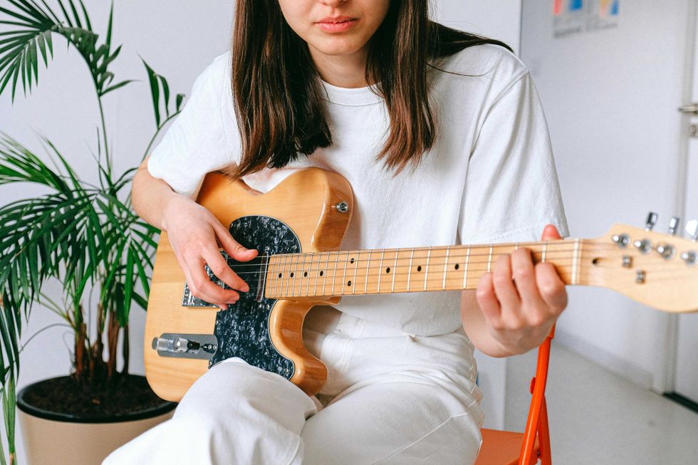 Person playing an electric guitar indoors, next to a potted plant.