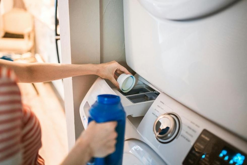 Person pouring detergent into a washing machine drawer.