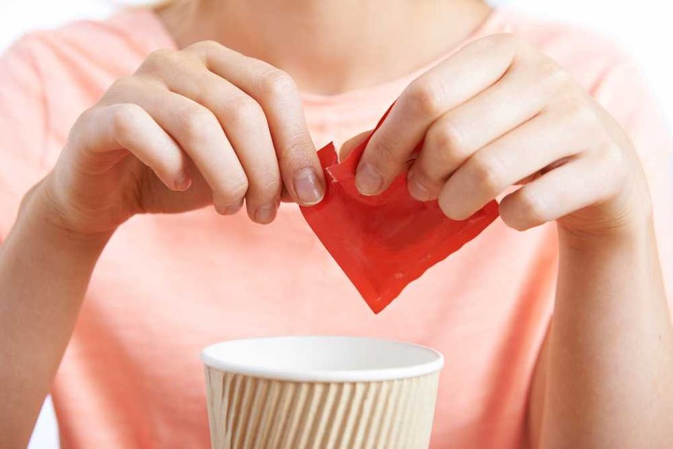 Person pouring sweetener from red packet into a paper cup.