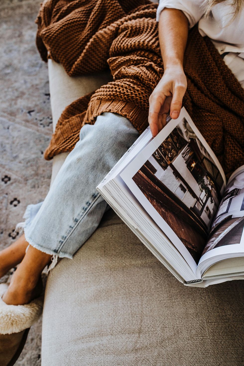 Person reading a book on a couch, wrapped in a brown blanket.