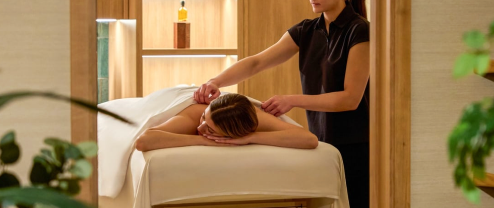 Person receiving a back massage in a tranquil spa setting with plants and warm lighting.