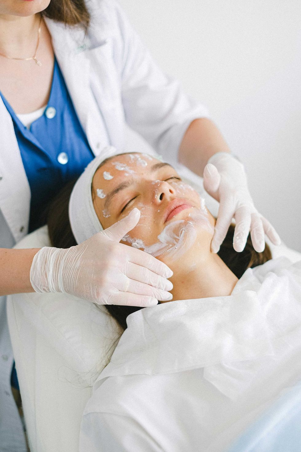 Person receiving a facial treatment, with cream applied, in a spa setting.