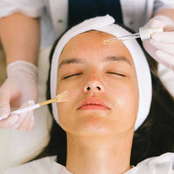 Person receiving a facial treatment with serum and brush applied on forehead.