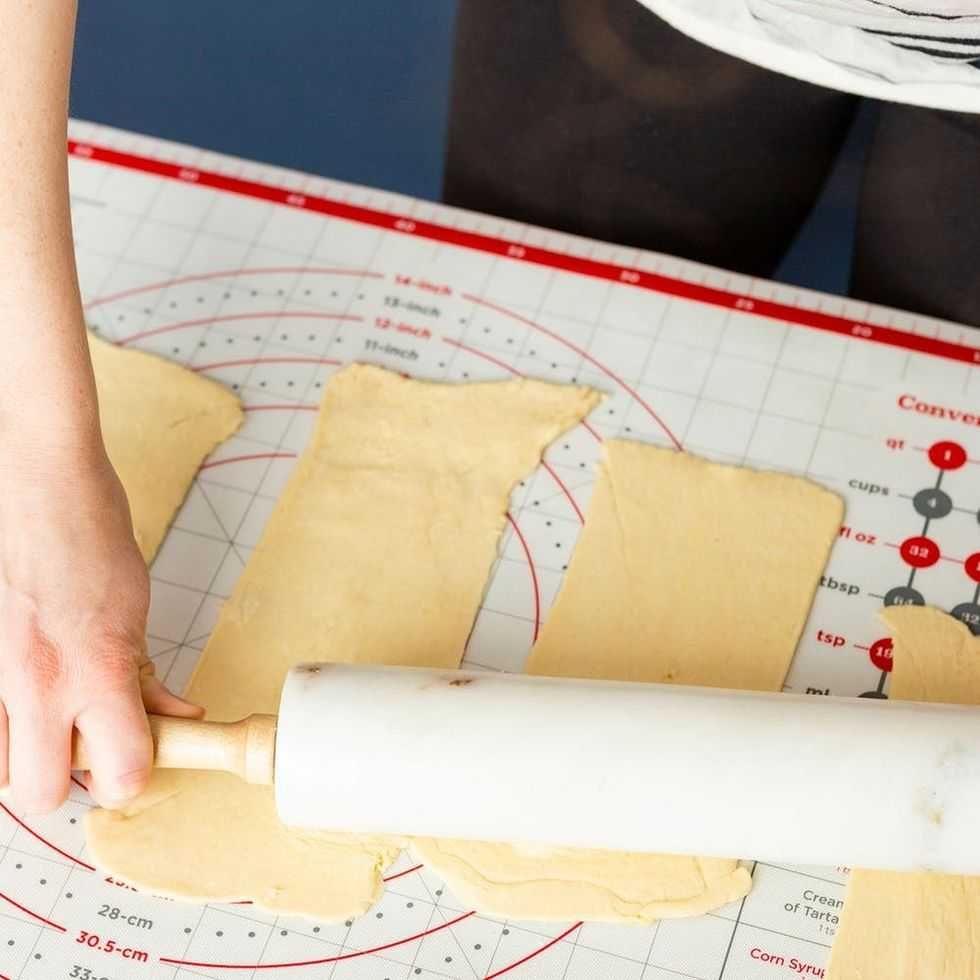 Person rolling out dough on a measurement mat with a marble rolling pin.