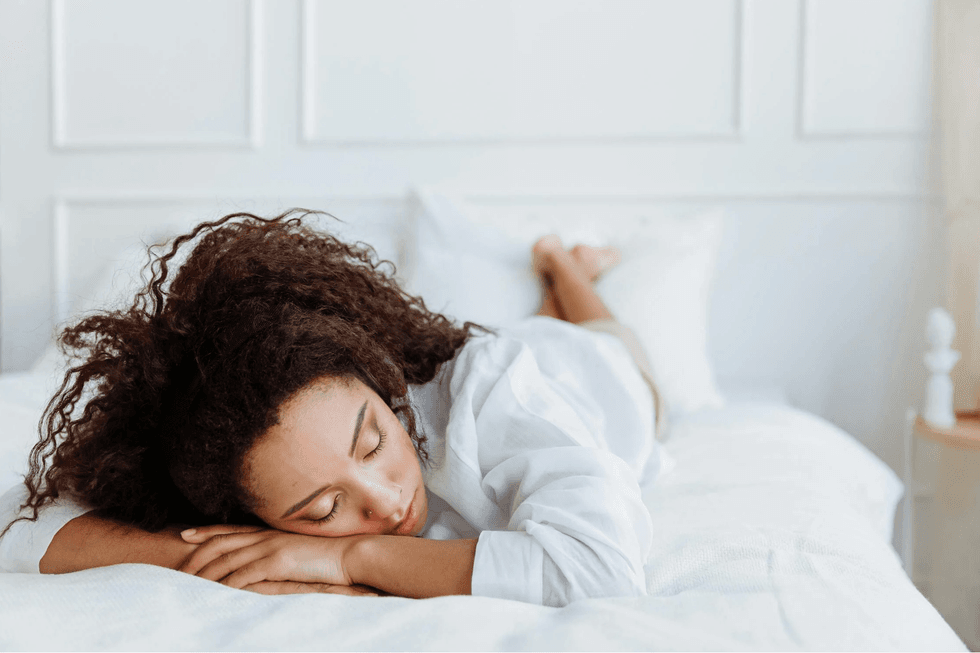 Person sleeping peacefully on a white bed in a bright room.