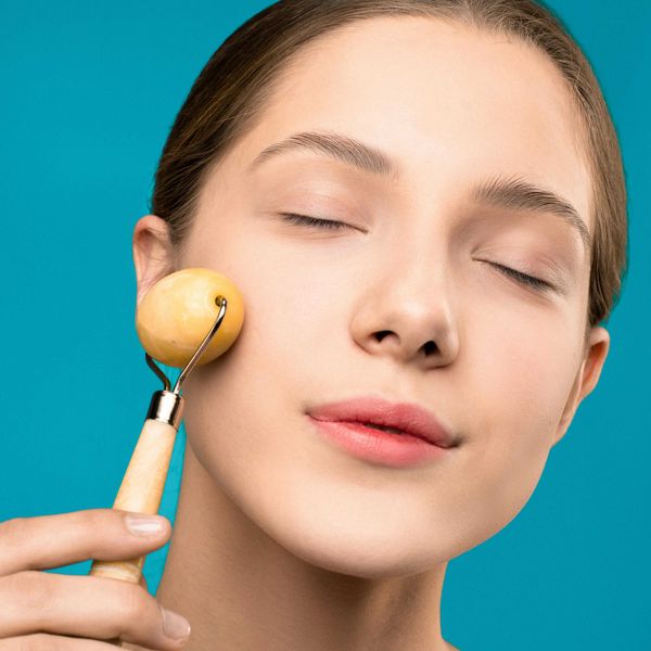 Person using a facial roller on their cheek against a blue background.