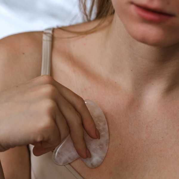 Person using a gua sha stone on their upper chest in a light camisole.