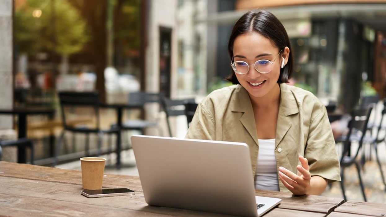 Person using a laptop at an outdoor café, with phone and coffee cup nearby.
