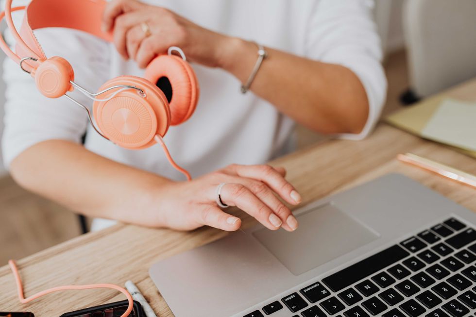 Person using a laptop touchpad while holding orange headphones in a home office setting.