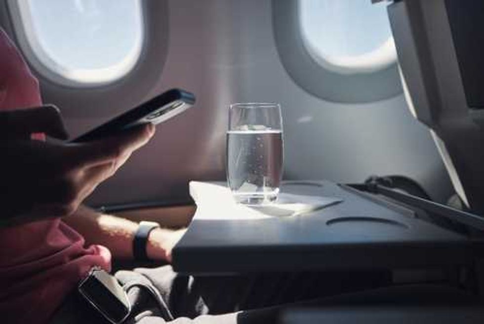 Person using phone on plane, glass of water on tray table.