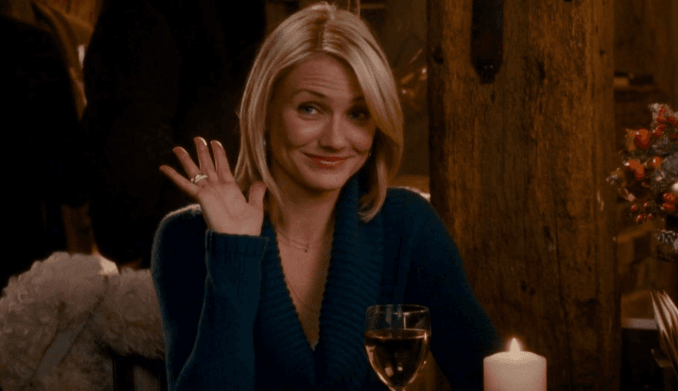 Person waving in a cozy setting with a wine glass and candle on the table.